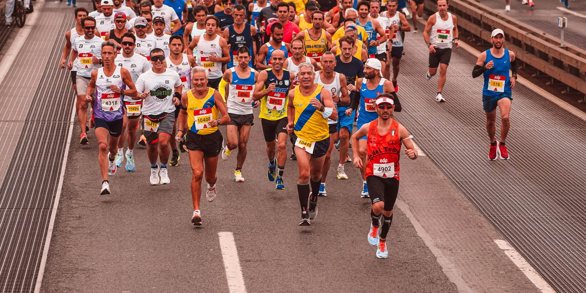 The front of a marathon field running toward the camera, with detection boxes on runners' faces and on their race bibs